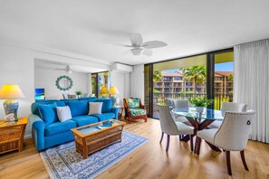 A modern living room with a blue sofa, glass coffee table, and a dining area with a glass table and chairs.