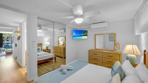 Een slaapkamer met een bed, een plafondventilator, een televisie, een dressoir en een spiegel.