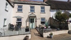 A two-story building with a green door, a small porch with chairs, and a sign indicating a tea garden. - Tea Cosy Cottage (Bude)