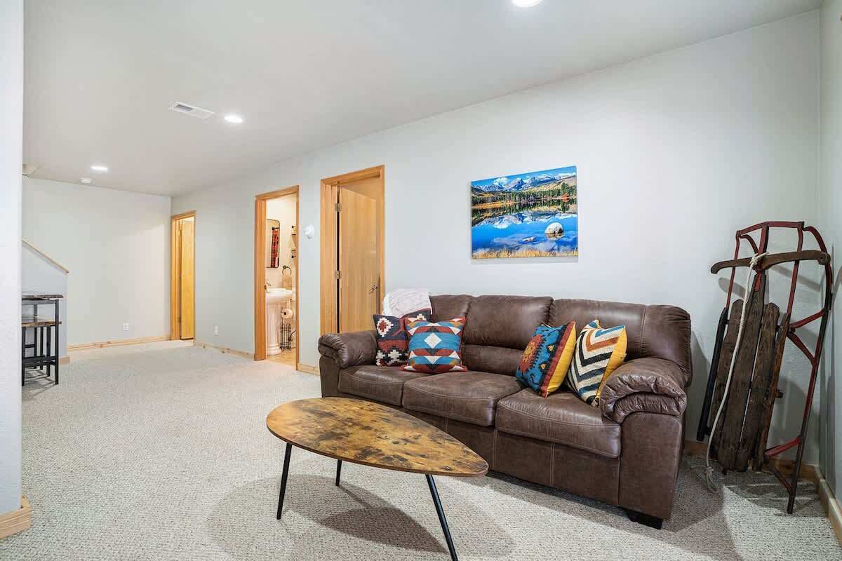 A living room with a brown leather sofa, colorful pillows, a wooden coffee table, and a painting of a snowy landscape.