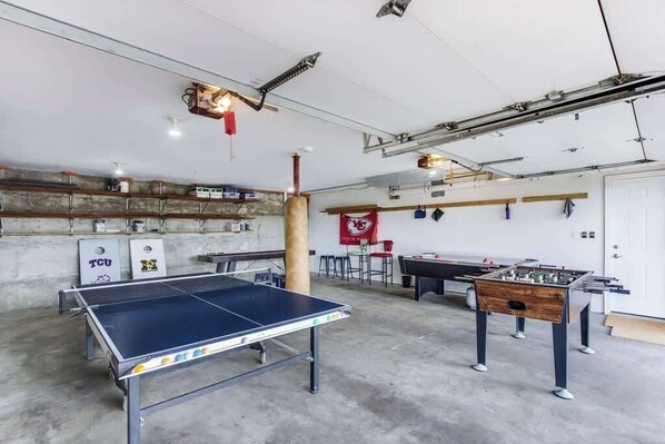 A recreational room with a ping pong table, foosball table, and a foosball table with a wooden base.