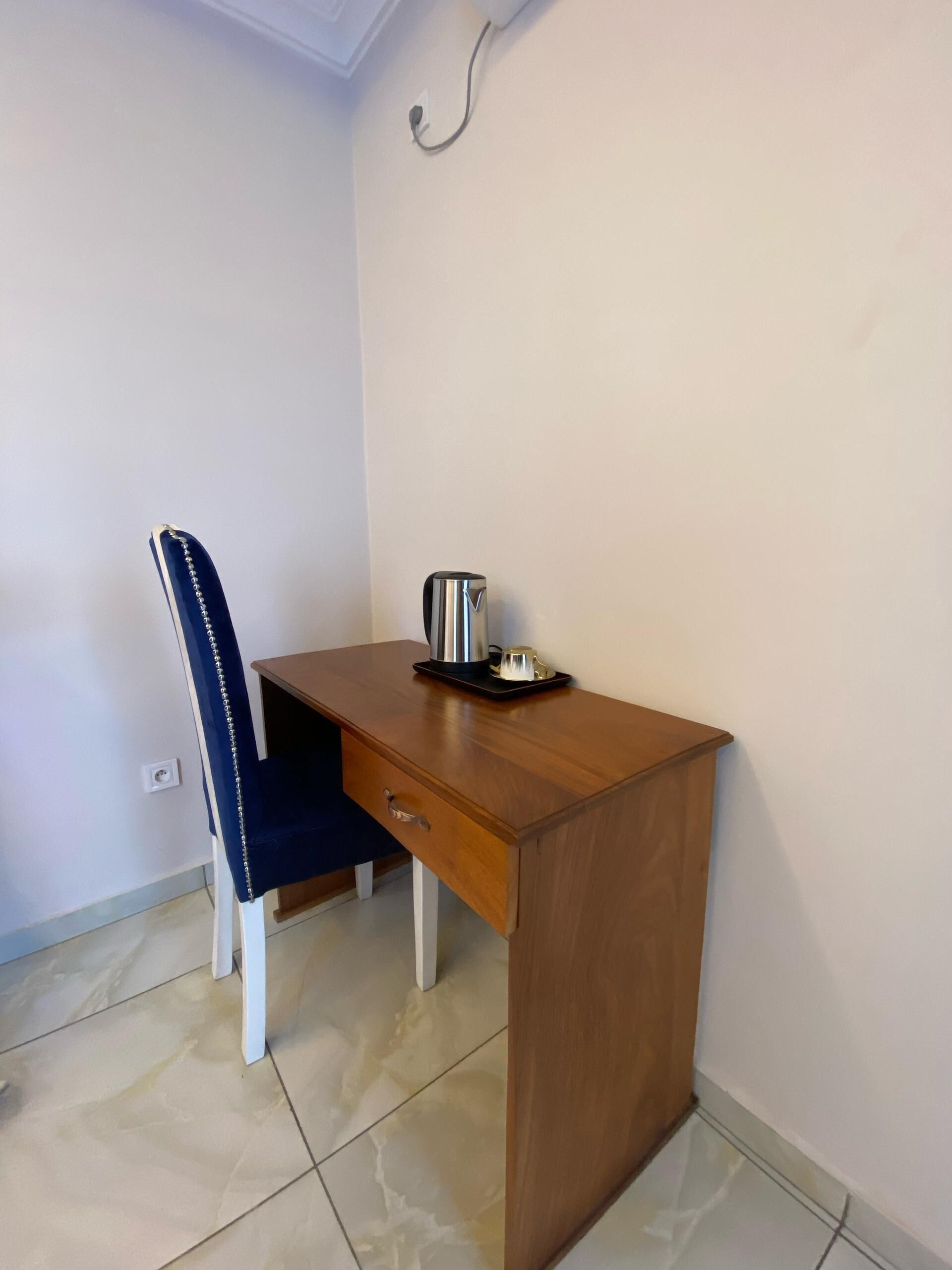 Una habitación pequeña y ordenada con un escritorio de madera, una silla y una tetera sobre el escritorio.