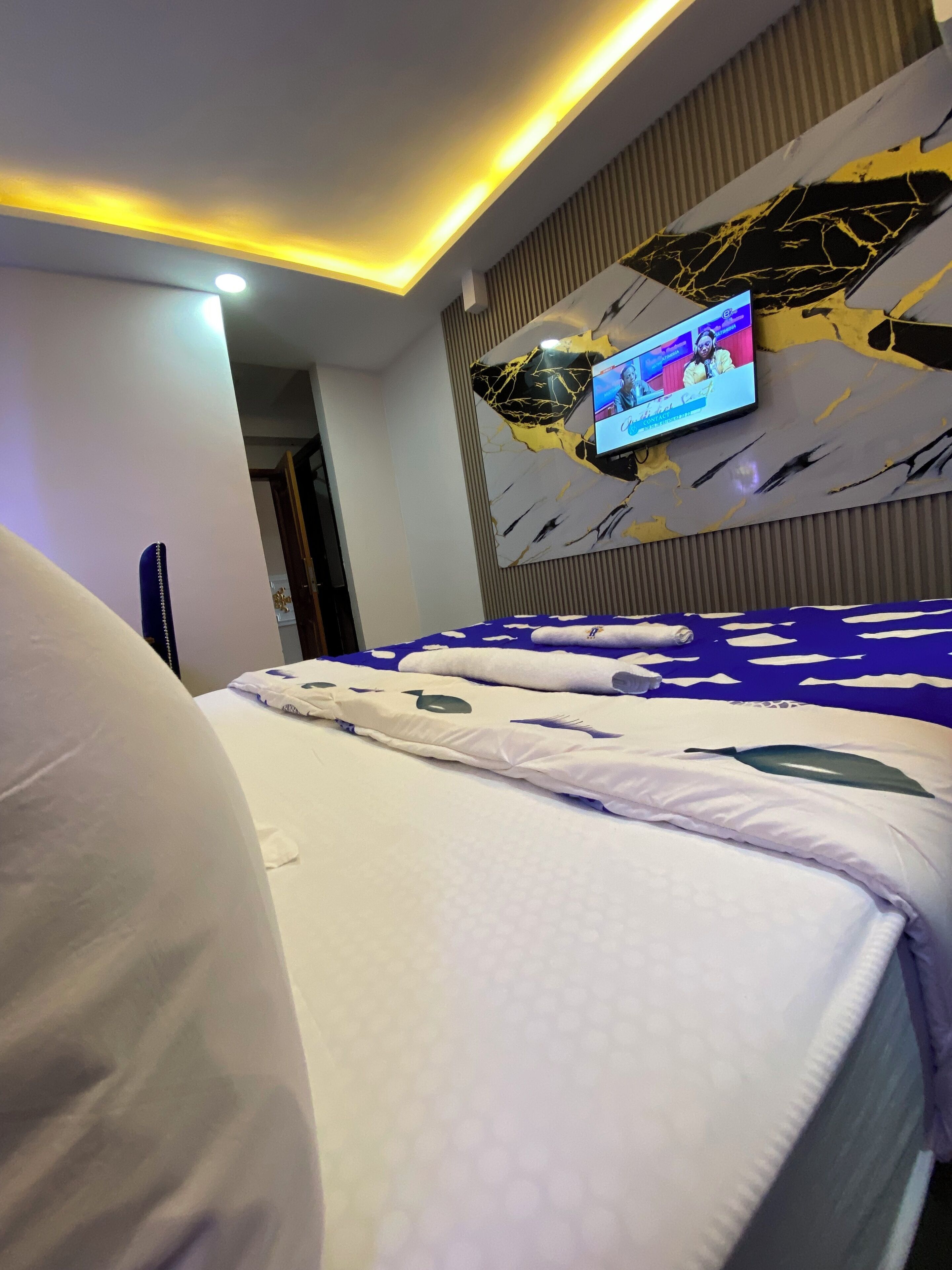 A modern hotel room with a bed, a flat-screen TV mounted on the wall, and a ceiling with recessed lighting.