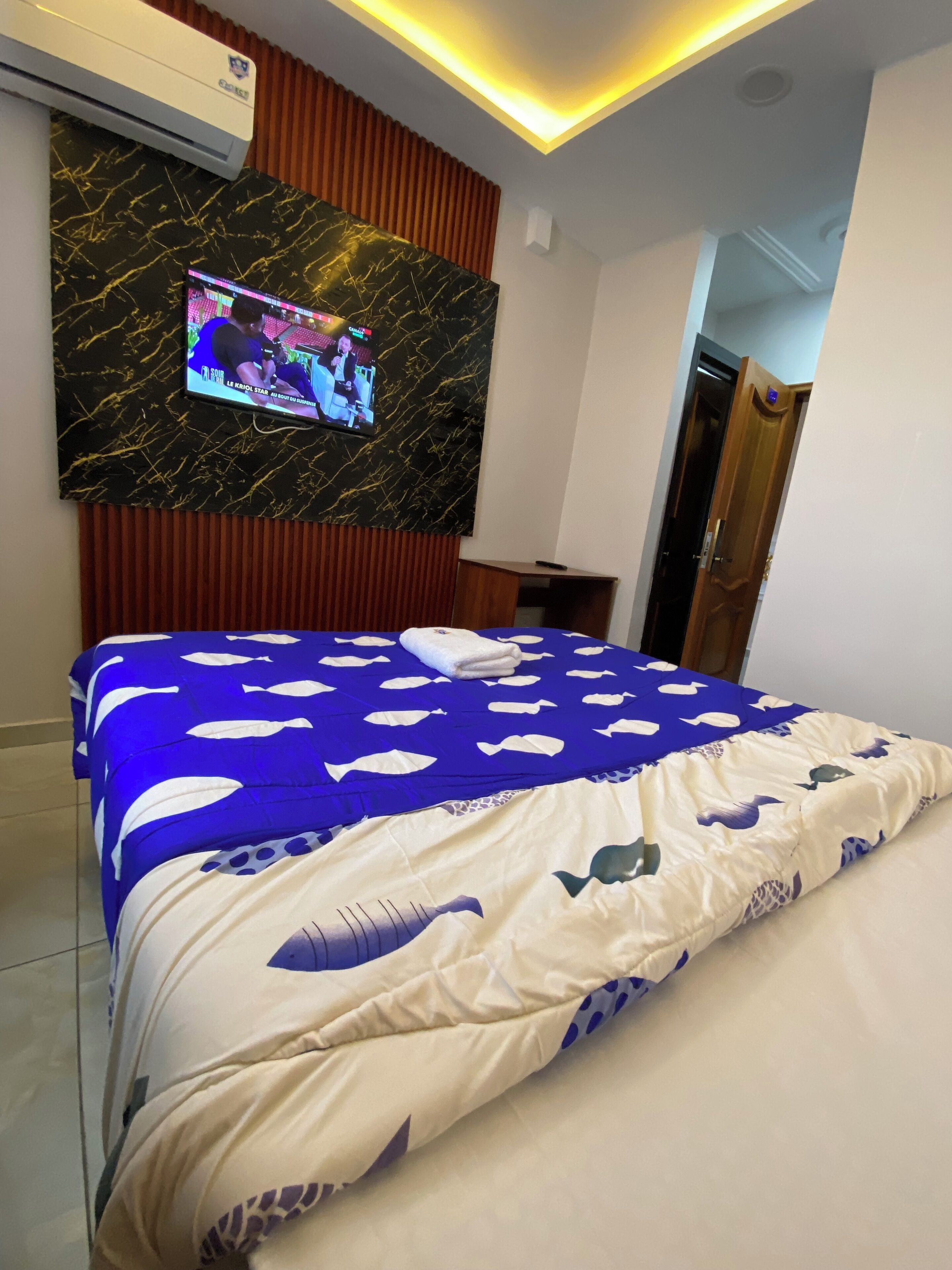 A hotel room with a bed, a TV mounted on a marble wall, and a wooden door.