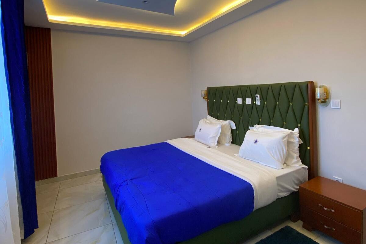A hotel room with a bed, a nightstand, a green headboard, and a ceiling with recessed lighting.