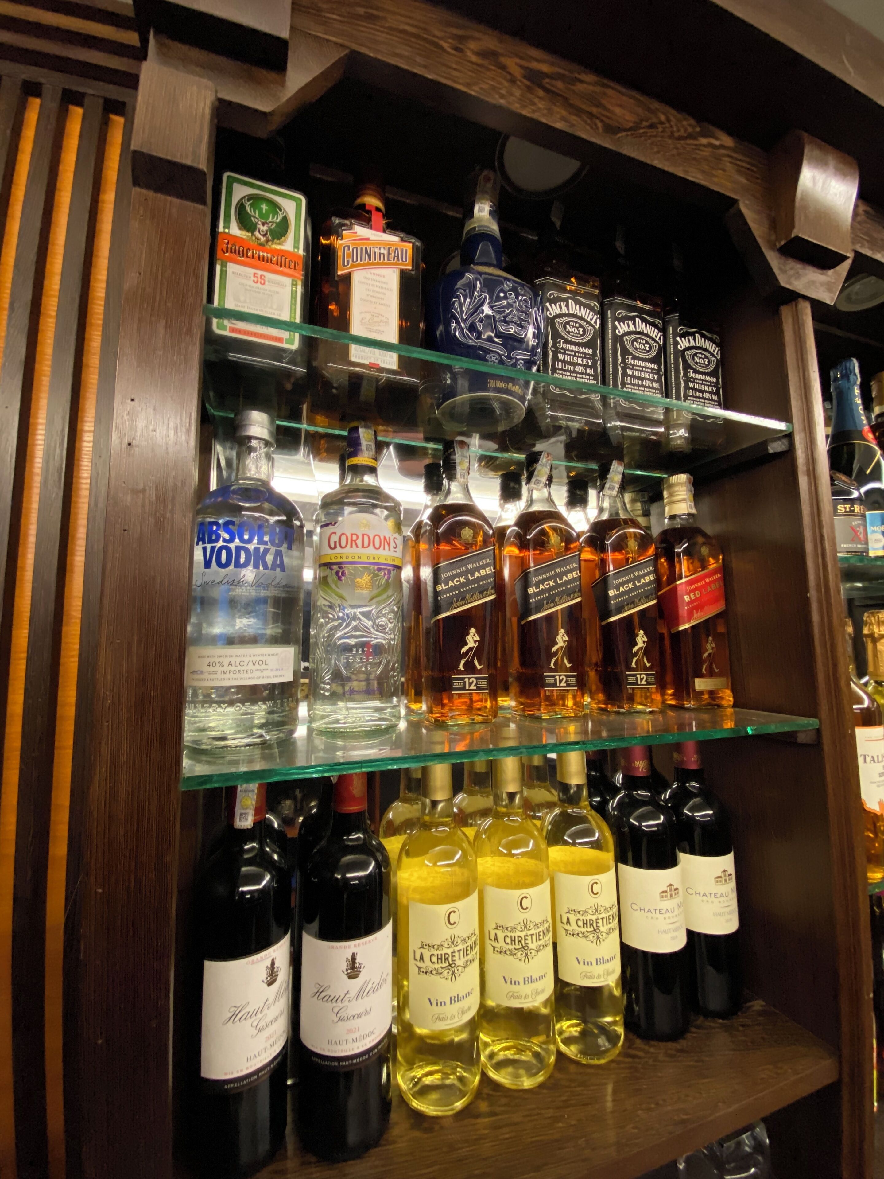 En butikshylde i en købmand fyldt med forskellige flasker alkohol, herunder vodka, whiskey og vin.