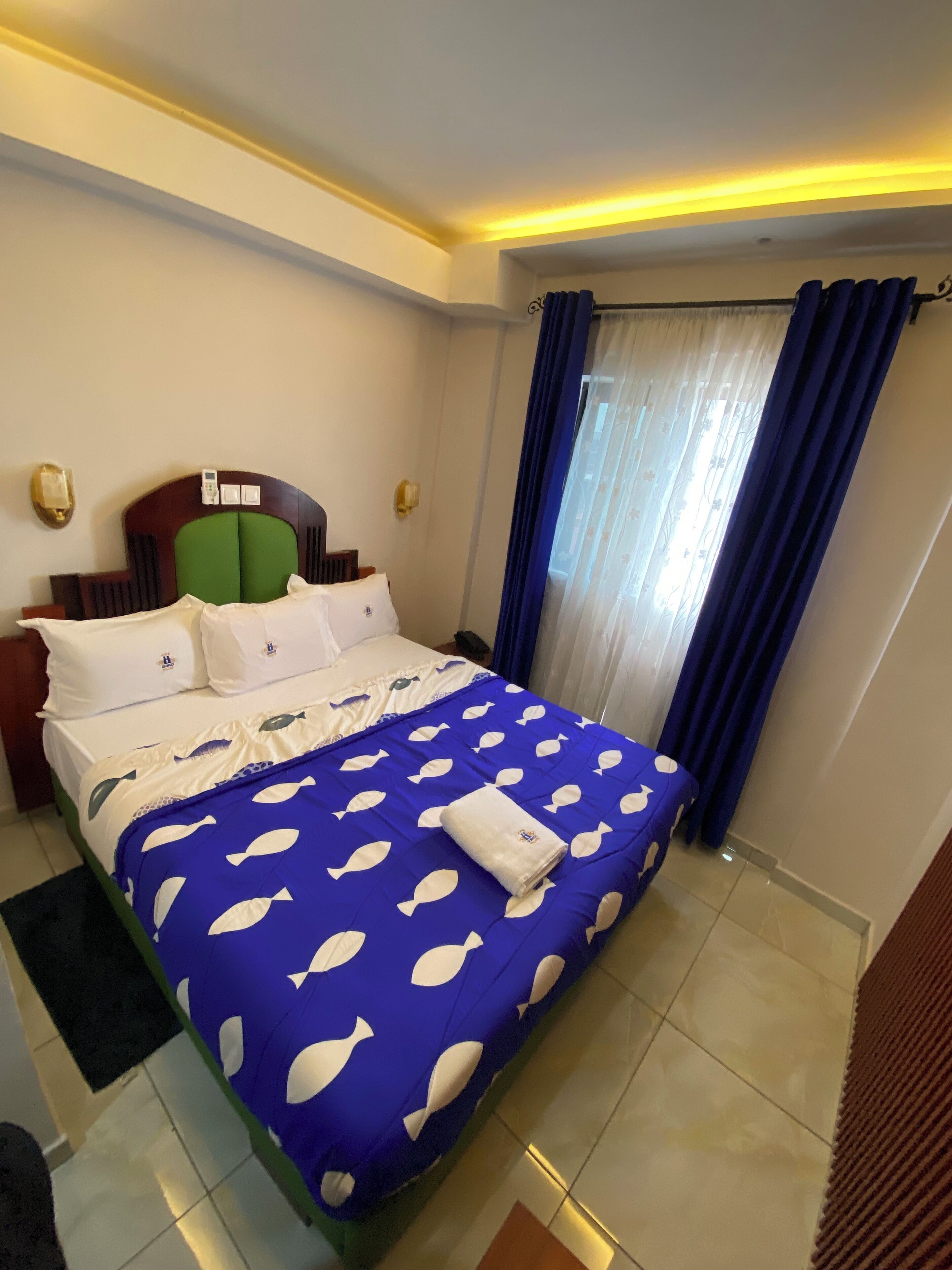 A hotel room with a bed, a nightstand, a wall-mounted phone, and a window with curtains.