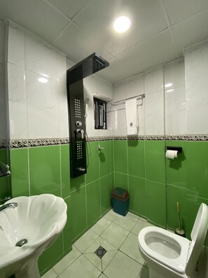 A bathroom with a toilet, sink, shower, and green tiled walls. - Guiko Palace Hôtel (Douala)