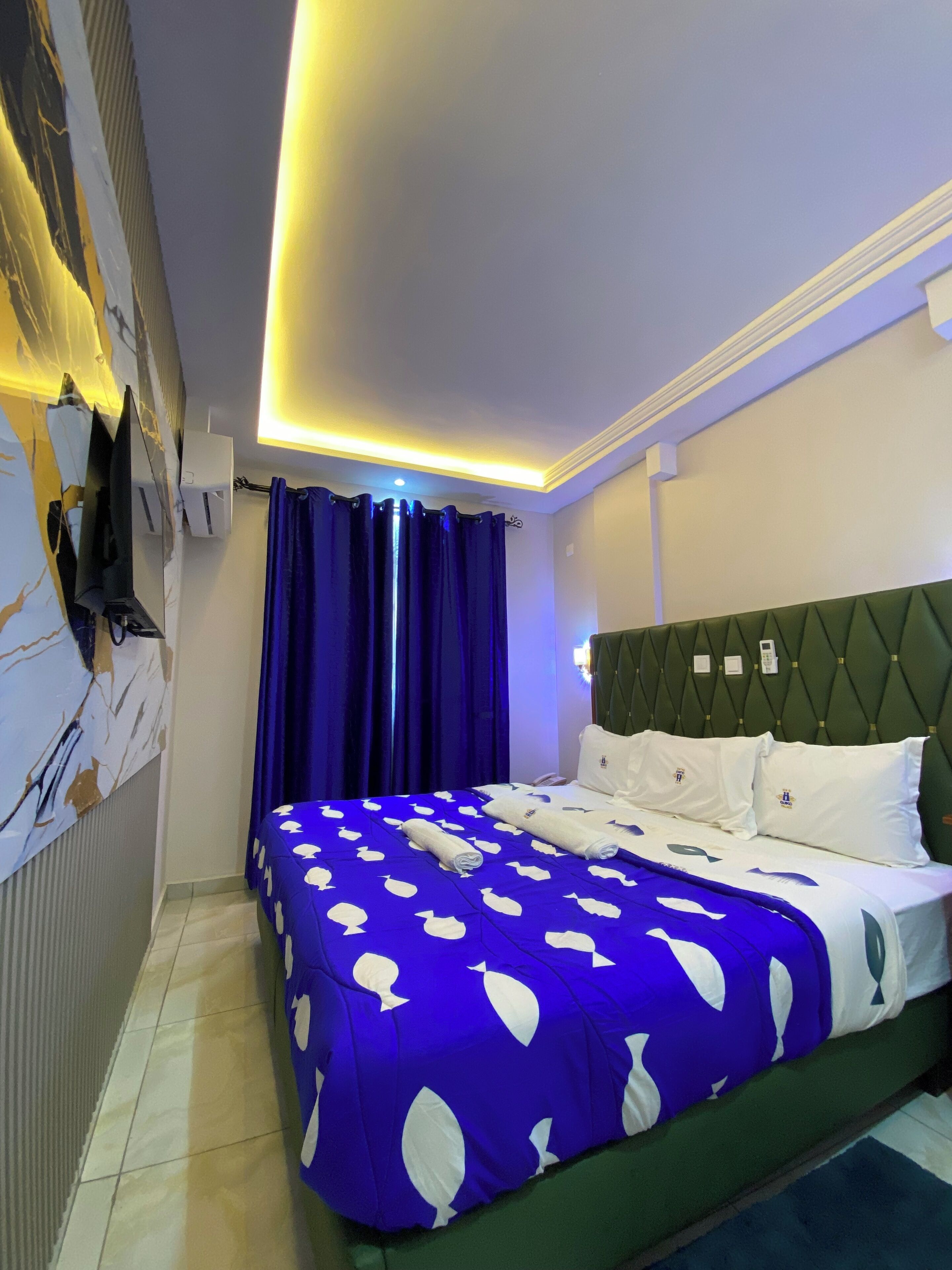 Una habitación de hotel con una cama, cabecera verde y cortina azul.