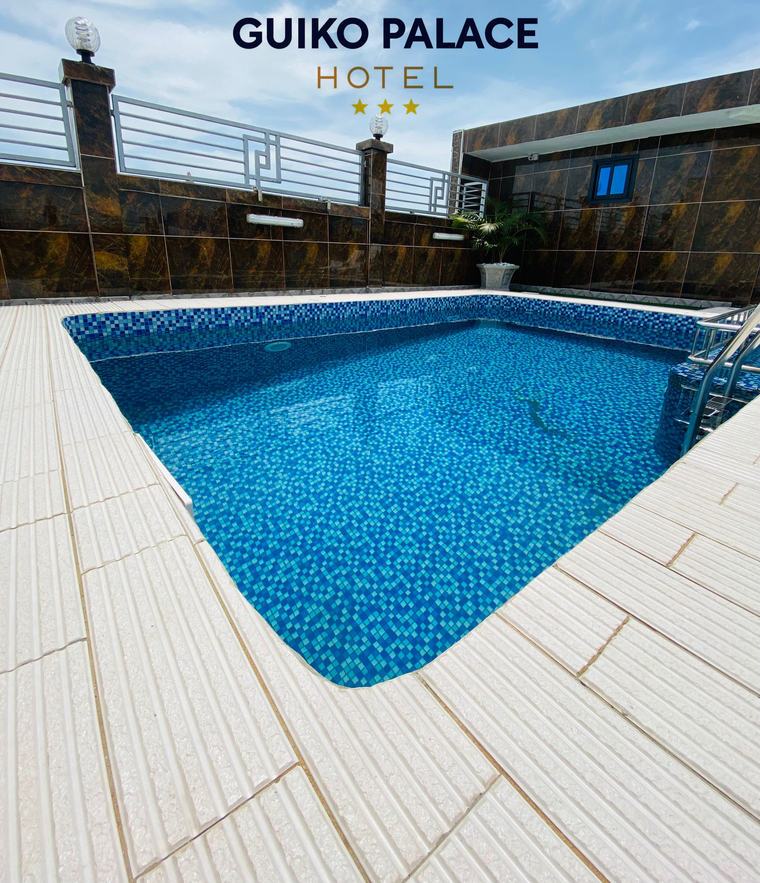 Área da piscina no GuiKo Palace Hotel, com piso ladrilhado e piscina azul cristalina.