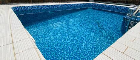 A pool area at GuiKo Palace Hotel with a tiled floor and a clear blue pool.