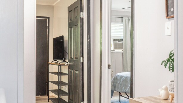 A hallway with a wooden floor, a television on a stand, and a bed in the distance. - Kick back and relax in this calm, stylish space. (Abilene)