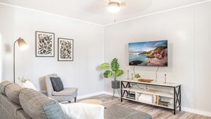 A modern living room with a grey sofa, a single armchair, a coffee table, a floor lamp, a TV mounted on the wall, and a console table with a plant and books. - Kick back and relax in this calm, stylish space. (Abilene)