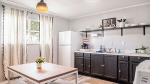 A modern kitchen with dark cabinets, a white refrigerator, and a wooden table with a plant. - Kick back and relax in this calm, stylish space. (Abilene)