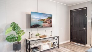 A living room with a mounted TV, a wooden console table, a potted plant, and a dark door. - Kick back and relax in this calm, stylish space. (Abilene)
