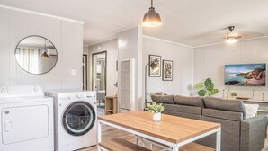 A modern living room with a sofa, a wooden table, a washing machine, and a TV mounted on the wall. - Kick back and relax in this calm, stylish space. (Abilene)