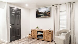 Una habitació amb una porta de fusta fosca, un armari de fusta ple de llibres i objectes decoratius, una cadira i un quadre d'un paisatge de muntanya.