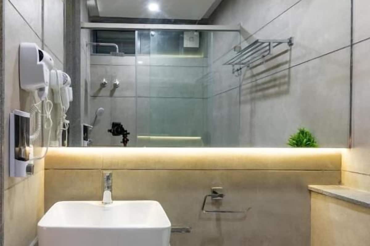 Un baño moderno con un espejo grande, un lavamanos blanco y una zona de ducha.