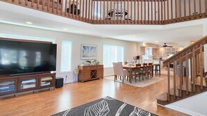 Amplia sala de estar con una escalera de madera, una mesa de comedor y un televisor de pantalla plana.