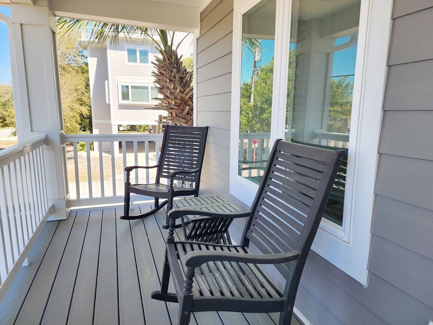 A wooden porch with two rocking chairs and a glass door leading to a balcony.