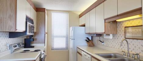 A compact kitchen with a stove, microwave, refrigerator, and sink.