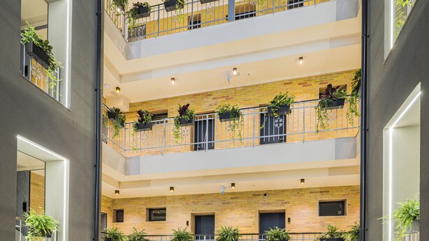 A multi-level hotel lobby with a dining area, multiple balconies with plants, and a modern interior design.