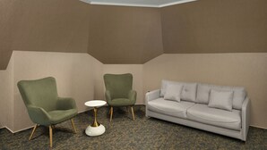 A room with a grey sofa, two green armchairs, and a small white table.