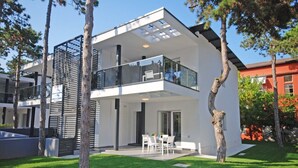 A modern two-story house with a balcony, a dining area, and a well-maintained lawn.