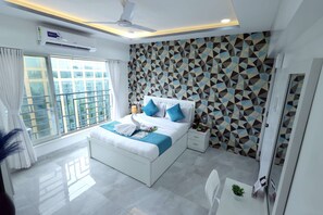 A modern bedroom with a bed, a ceiling fan, a window with curtains, and a geometric patterned wall. - 1 BHK Suite ( Gagal Home) (Mumbai)