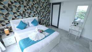 A modern hotel room with a geometric-patterned wall, a large bed with white bedding and blue pillows, a bedside table with a lamp, and a small desk with a mirror and a plant. - 1 BHK Suite ( Gagal Home) (Mumbai)