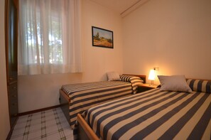 Ein Zimmer mit zwei Betten, einem Nachttisch, einer Lampe, einem Fenster mit Vorhängen und einem Bild an der Wand.