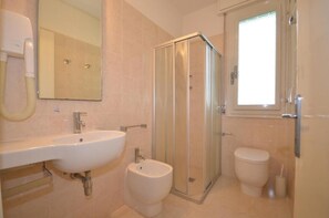 Un baño con lavamanos, bidé, inodoro y ducha con mampara de vidrio.
