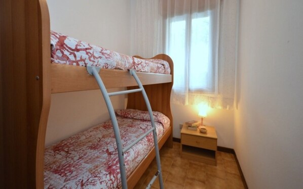 Un lit superposé avec une échelle, une table de chevet avec une lampe et une fenêtre avec des rideaux.