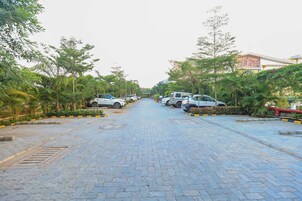 Uma estrada pavimentada flanqueada por carros estacionados e vegetação exuberante, que conduz a um edifício com arquitetura clássica.