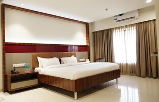 Quarto de hotel com uma cama grande, mesa de cabeceira com telefone e garrafas de água, ar condicionado fixado na parede e janela com cortinas.