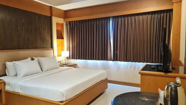 Ein Hotelzimmer mit einem großen Bett, einem Schreibtisch mit Wasserkocher und einem Fernseher.