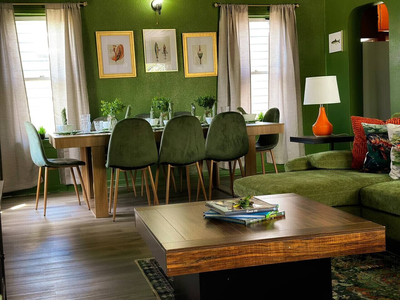 Un comedor con una mesa y sillas de madera, un sofá verde y cuadros en la pared.