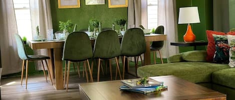 A dining area with a wooden table and chairs, a green sofa, and framed artwork on the wall.