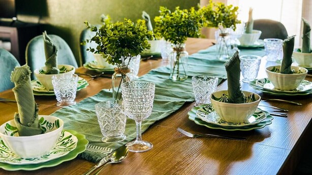 A dining table set with glassware and plants, with chairs around.