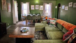 A cozy living room with a green sofa, a coffee table, and a dining area with chairs and a table.