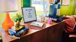 A desk with a lamp, a welcome sign, books, a notebook, a coffee maker, and a laptop.