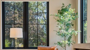 Una sala de estar moderna con un ventanal grande, un sillón de cuero, una mesita con una lámpara, una planta en maceta y un mueble de madera.