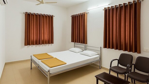 Une chambre d’hôtel avec un lit, deux ventilateurs de plafond, des rideaux marron, une petite table et deux chaises.