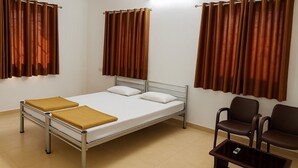 Une chambre avec un lit simple doté d’un cadre en métal, de deux oreillers, d’un coussin marron et d’une table de chevet en bois avec une télécommande.
