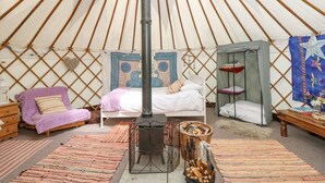 A cozy interior of a round yurt with a bed, a seating area, a small table, and a heater. - Stardust (Ventnor)