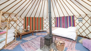 Interior de una yurta con un poste de madera central, una cama, una mesita con un farolillo y tejidos a rayas de colores en las paredes.