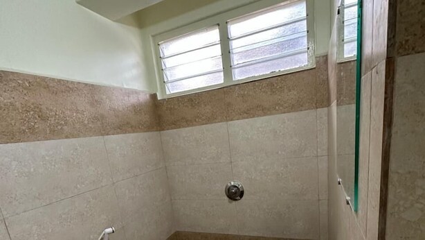Une petite salle de bain avec des toilettes, un lavabo et une douche. Il y a une fenêtre au-dessus des toilettes et un miroir sur le mur.