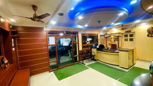 Un espace d’accueil avec un comptoir en bois, un ventilateur de plafond et une moquette verte.