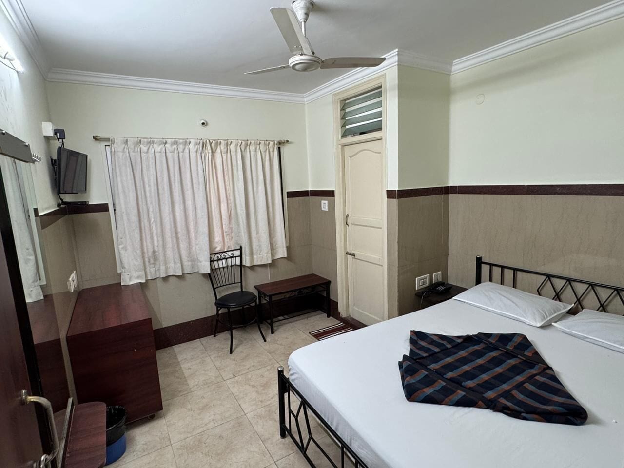 A hotel room with a bed, a desk, a chair, a television, and a ceiling fan.