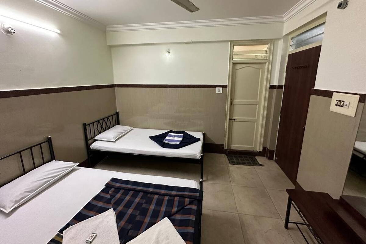 A small, clean room with two single beds, a ceiling fan, and a door leading to another room.